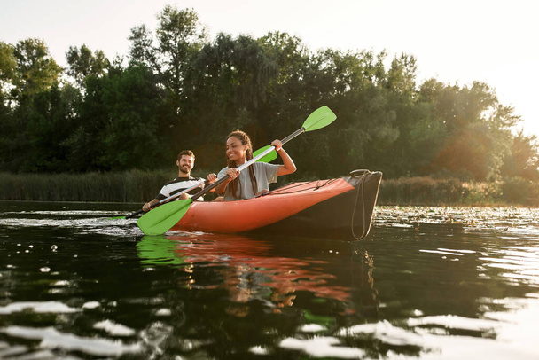 Young couple of friends having fun, kayaking in a river surrounded by the beautiful nature on a summer day - Photo, Image