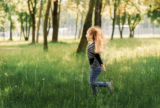 Mała dziewczynka radośnie biega po trawie w parku latem - Zdjęcie, obraz