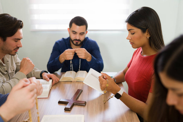 Διαφορετική ομάδα νέων ανθρώπων σε μια θρησκευτική κοινότητα προσεύχονται με ένα καθολικό κομπολόι κατά τη διάρκεια της ομάδας μελέτης της Βίβλου τους  - Φωτογραφία, εικόνα