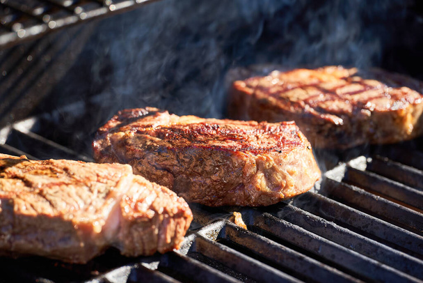Biefstuk vlees koken op de grill. Rook stijgt op uit het rooster. - Foto, afbeelding