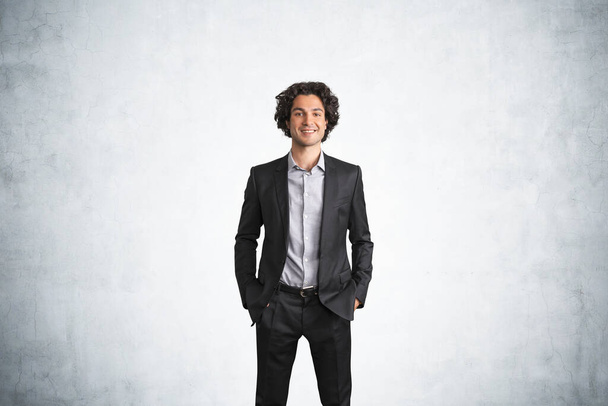 Office man in black business suit smiling with curly hair. Confident manager in office room with mockup copy space blank wall, concept of business worker and boss - Foto, Imagen