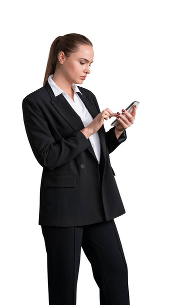 Side view of young attractive business woman in black suit with white shirt holding smartphone and browsing the internet, isolated on white background - Photo, Image