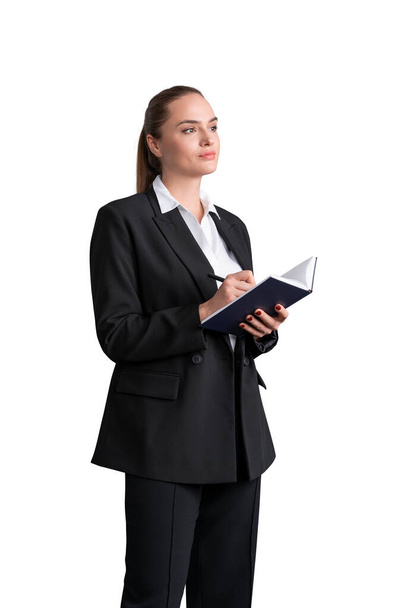 Attractive business woman in formal suit and shirt is holding a planner and pen, taking notes, looking forward and dreaming about future corporate career prospectives. Isolated over white background - Photo, image