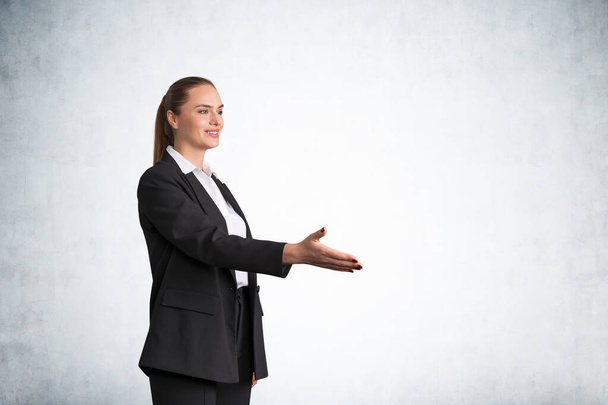 Office woman smiling offer hand to shake, boss in black office suit, copy space empty concrete wall. Concept of agreement and business deal - Photo, image