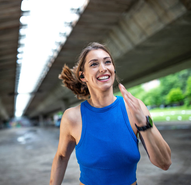 Young woman running jogging fast outdoors. Female athlete smiling exercising under bridge.  - Photo, Image