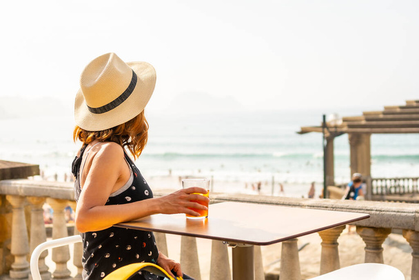 Summer vacation lifestyle. Young caucasian girl in a hat having a soda next to the beach - Zdjęcie, obraz