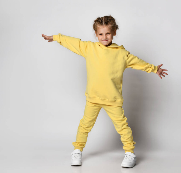 Full length portrait of a little girl dressed in a bright yellow sports suit. - Photo, image