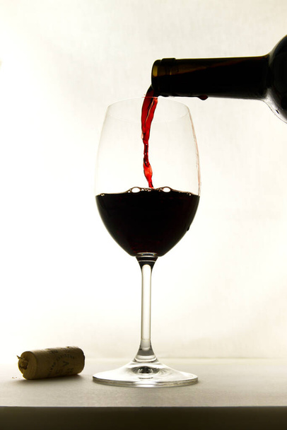 Silhouette of a wine glass in which they are putting red wine from the bottle directly, the background is white and the glass is isolated - Photo, Image