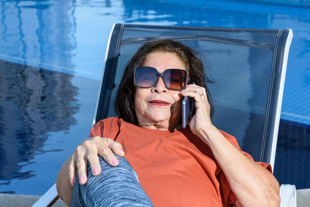 Крупним планом 74-річна жінка з сонцезахисними окулярами сидить і відповідає на дзвінок
. - Фото, зображення