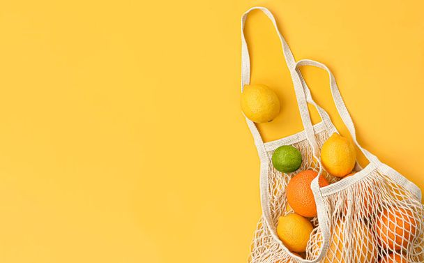 Свежие апельсины, лимоны, лаймы и грейпфруты в сетчатом мешке на желтом фоне - Фото, изображение