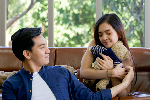 Young lovers spend time together on holidays in the living room. The young man wears comfortable clothes, hand a teddy bear to surprise girlfriend on special occasions. - Photo, Image