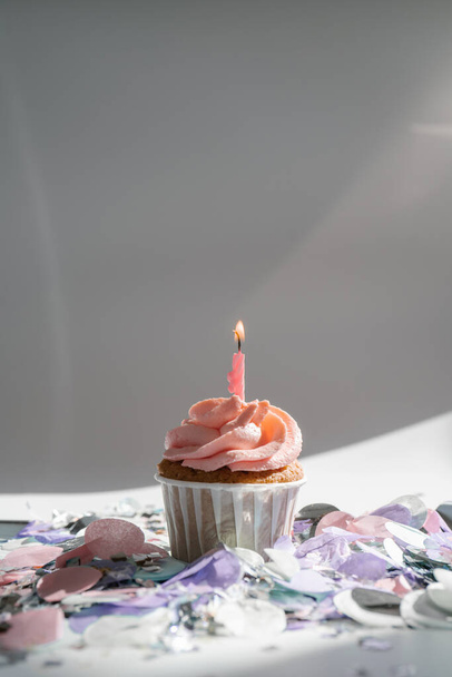 A cupcake with a candle stands on a white background with a shadow. - Φωτογραφία, εικόνα