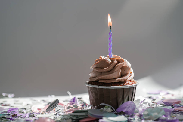A cupcake with a candle stands on a white background with a shadow. - Foto, Imagem