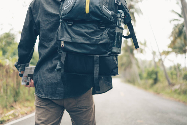 rear view of man with backpack hold passport and map hiking and walking on the road in forest. Backpack travel concept. - Fotografie, Obrázek