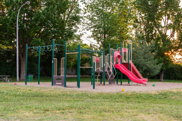 Παιδική χαρά χωρίς παιδιά στο τοπικό δημόσιο πάρκο. Παίξτε δομή με κόκκινες διαφάνειες το βράδυ του καλοκαιριού με ηλιοβασίλεμα. - Φωτογραφία, εικόνα