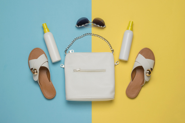 Sandales, crème solaire et un sac blanc sur fond jaune et bleu. Concept de vacances. Pose plate. - Photo, image