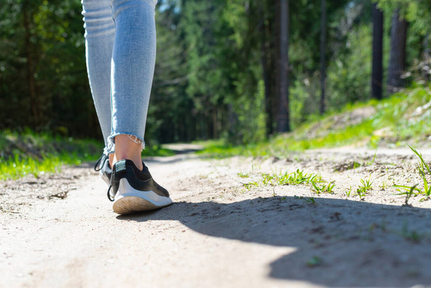 Vue arrière photo de jambes touristiques féminines avec des baskets marchant dans une route forestière.Soleil d'été. - Photo, image