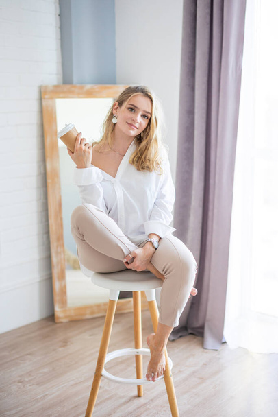 Portrait of a beautiful sensual young woman with blonde hair wearing a white shirt in home interior - Photo, Image