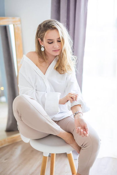 Portrait of a beautiful sensual young woman with blonde hair wearing a white shirt in home interior - Foto, Bild