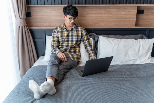 Un freelance di sesso maschile trascorrere del tempo a lavorare con i suoi computer portatili pacificamente sul suo letto. - Foto, immagini