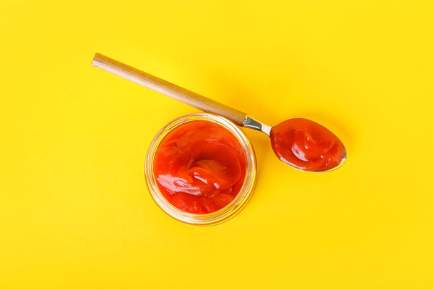 Tarro y cuchara con sabroso ketchup sobre fondo de color - Foto, Imagen