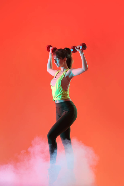 Sportliche junge Frau trainiert mit Kurzhanteln auf farbigem Hintergrund - Foto, Bild