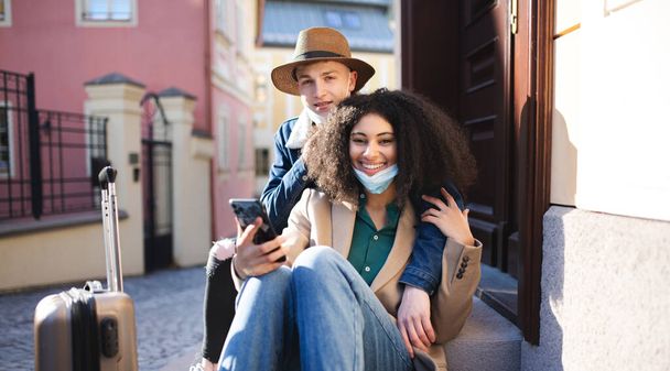 Young couple tourists with smartphone on holiday in old town, coronavirus concept. - Фото, изображение