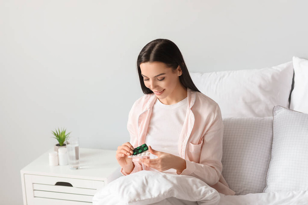 Beautiful young woman with pills in bedroom - Foto, afbeelding
