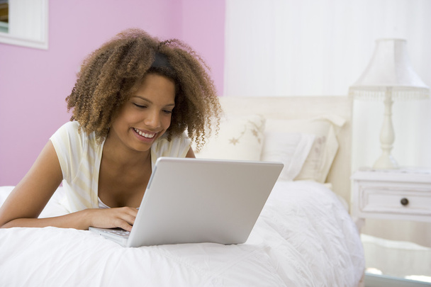 dospívající dívka leží na posteli pomocí přenosného počítače - Fotografie, Obrázek