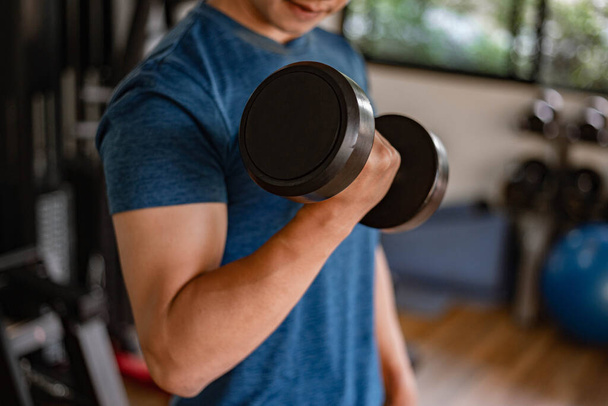 Training gym concept a young adult using his muscular strong arm lifting a dumbbell upward and downward in the gym. - Photo, image