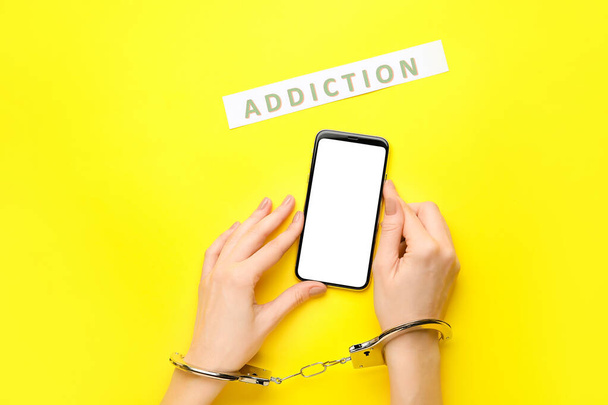 Woman with mobile phone and in handcuffs on color background. Concept of addiction to gadget - Photo, Image