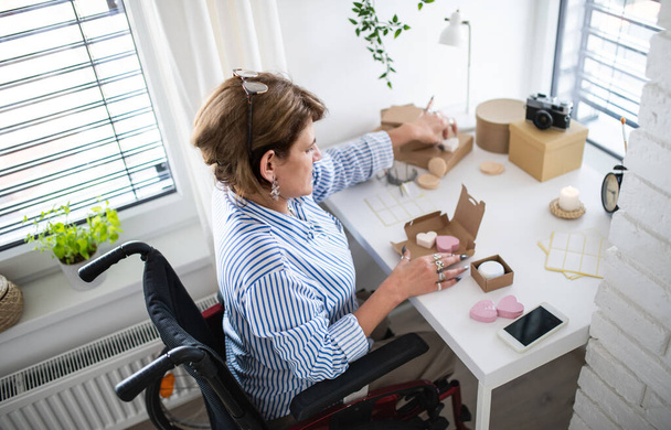 Disabled mature woman in wheelchair packing handmade products indoors at home, small business concept. - Φωτογραφία, εικόνα