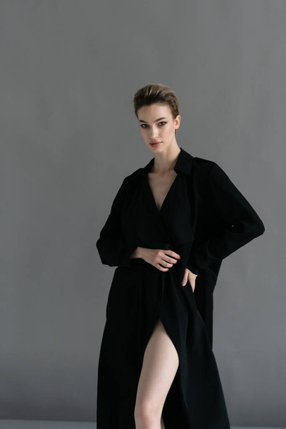 young beautiful woman posing in a black cloak in the studio - Фото, зображення