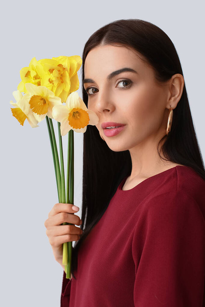 Beautiful young woman with narcissus bouquet on light background - Fotoğraf, Görsel