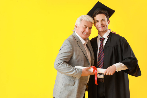 Feliz estudiante de graduación masculina con su padre en el fondo de color - Foto, Imagen