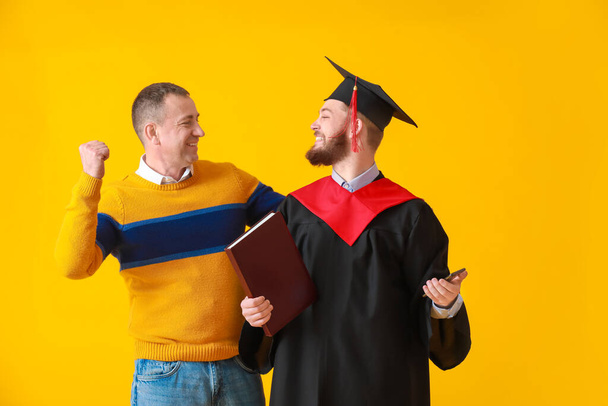 Feliz estudiante de graduación masculina con su padre en el fondo de color - Foto, Imagen