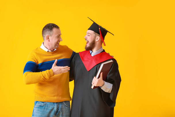 Happy male graduation student with his father on color background - 写真・画像