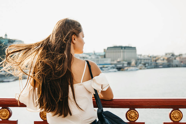 Γυναίκα με μακριά μαλλιά κοιτάζει το ποτάμι και την πόλη sca - Φωτογραφία, εικόνα