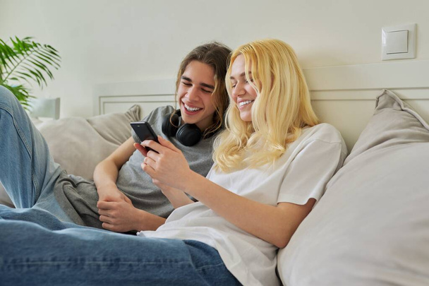 Happy laughing hipster teenagers male and female having fun using smartphone together - Foto, afbeelding