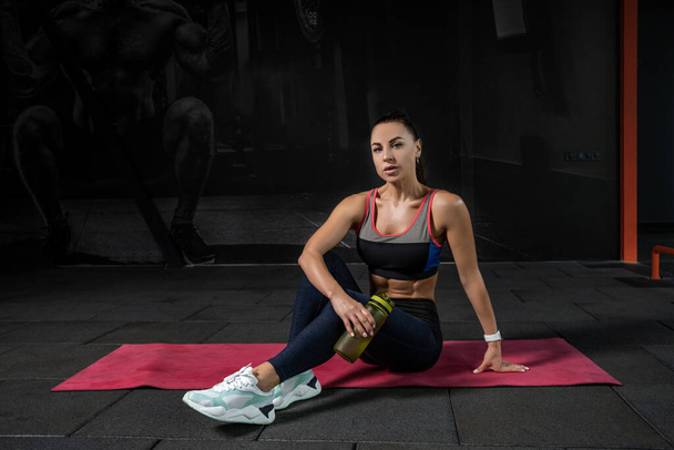 Sportos fiatal nő ül szőnyegen a modern tornateremben - Fotó, kép