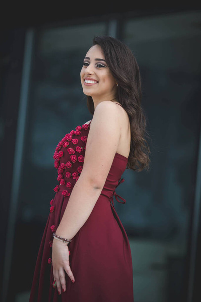 An attractive Caucasian female wearing an elegant burgundy dress on background of a building - Photo, Image