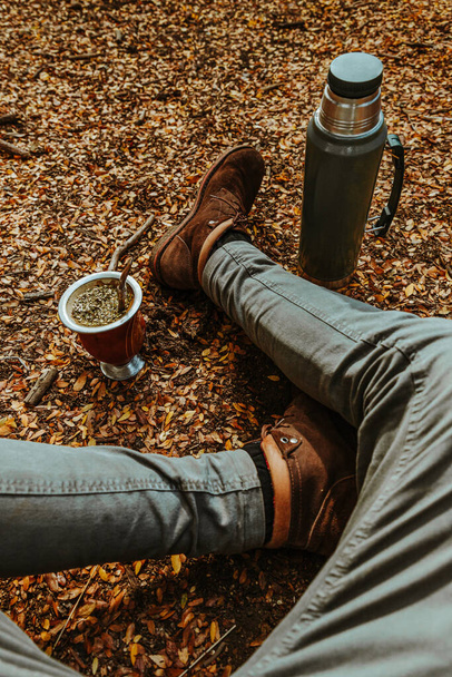 A man sitting on the ground covered with fallen leaves and enjoying mate drink - Φωτογραφία, εικόνα