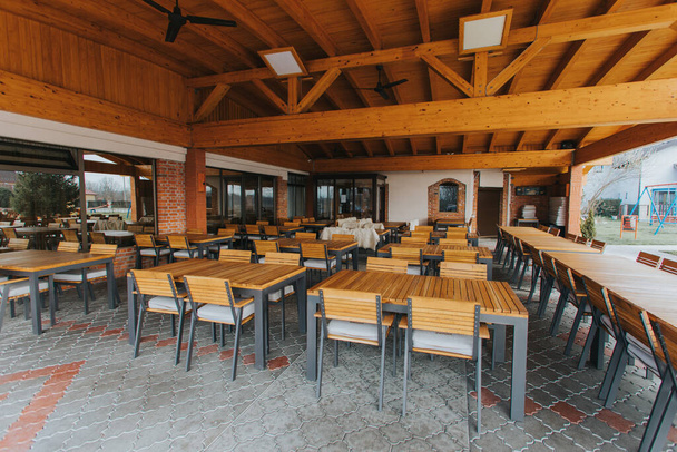 Открытое кафе с деревянными столами и стульями под навесом днем - Фото, изображение