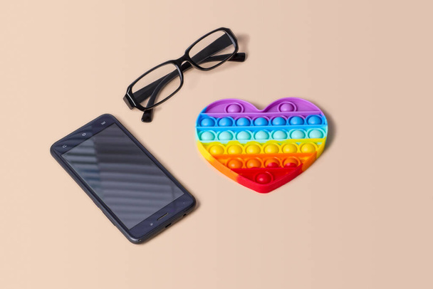 Silicona arco iris corazón antiestrés en un fondo con gafas y un teléfono - Foto, imagen