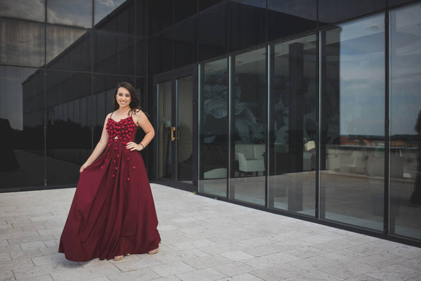 A young woman in long evening dress smiling and posing on the balcony - Foto, Imagen