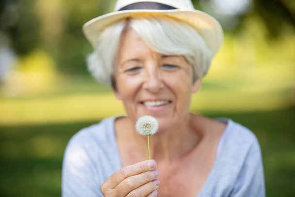 happy elderly woman senior blowing on a dandelion - Zdjęcie, obraz