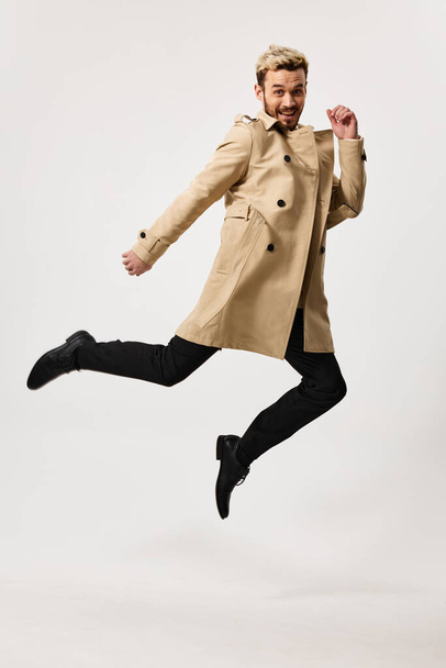 Fröhlicher Mann im beigen Mantel springt Emotionen isoliert Hintergrund - Foto, Bild