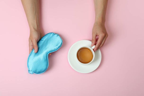 Γυναικεία χέρια κατέχουν μάσκα ύπνου και το τσάι σε ροζ φόντο - Φωτογραφία, εικόνα