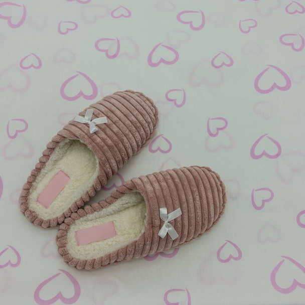 Soft pink plush indoor slippers decorated with bows. White background with hearts. Top view. Close-up - Foto, Imagem