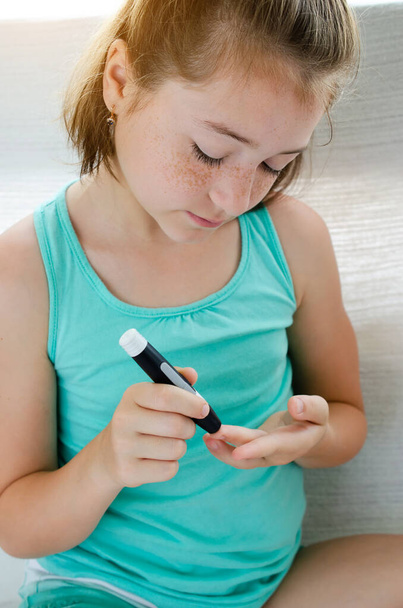 Маленька дівчинка перевіряє рівень цукру в крові, використовуючи ланцет і глюкометр вдома
. - Фото, зображення